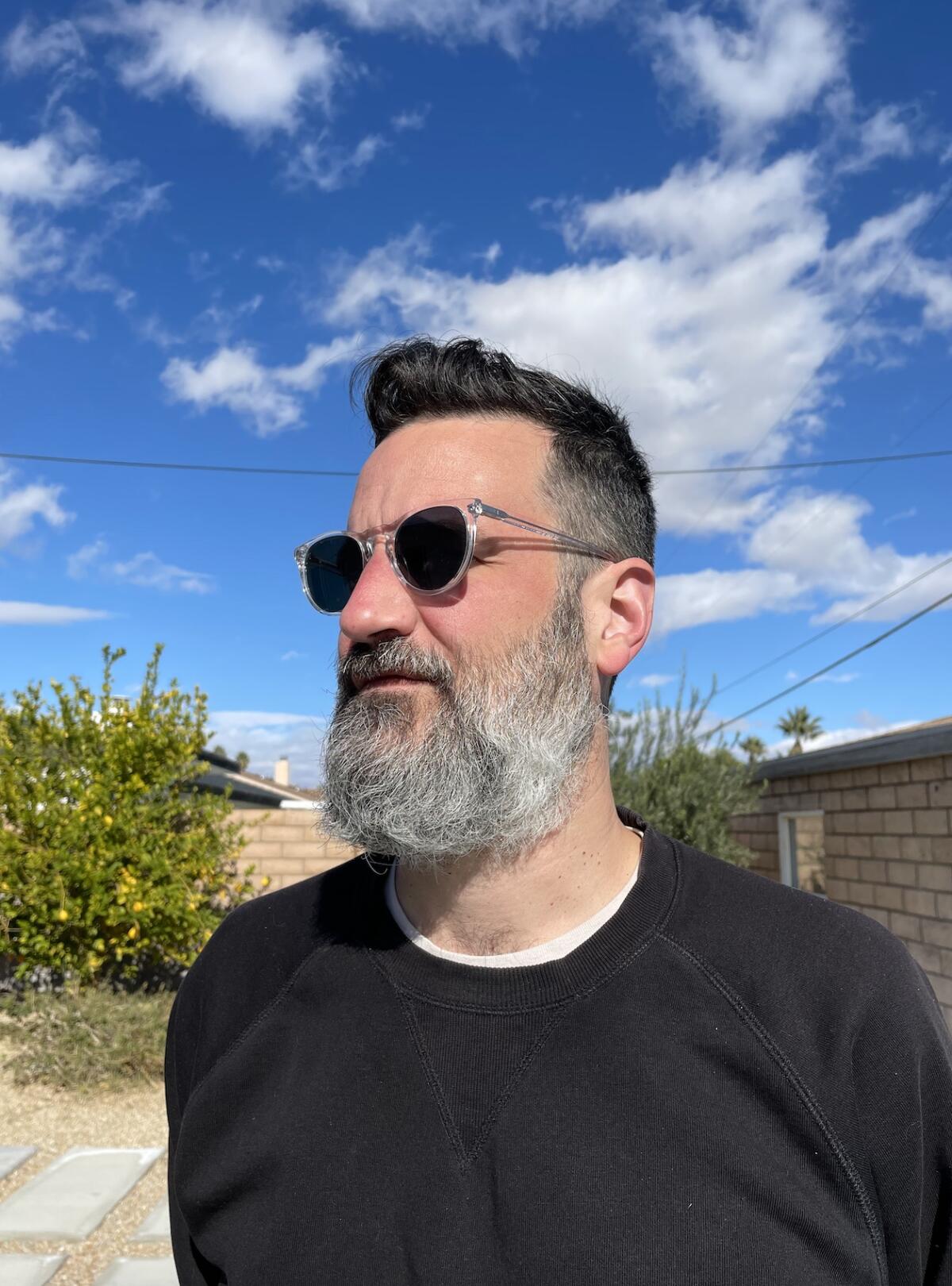 Man with a robust salt and pepper beard looking into the distance against a blue sky.