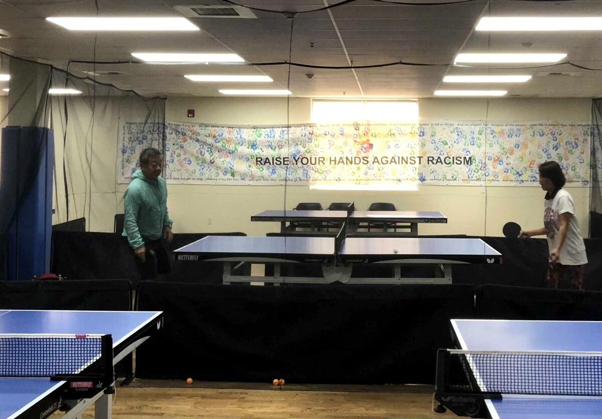 Leisure World residents play table tennis next to a banner that decries racism. 