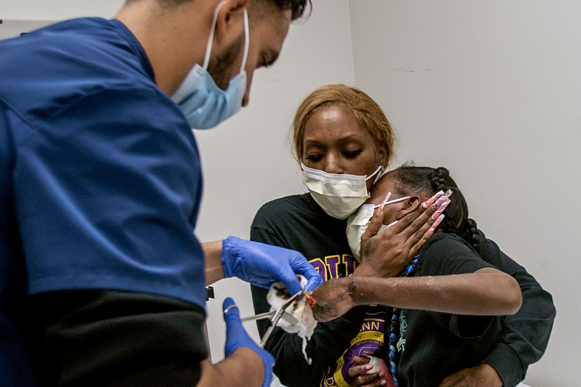 Staneisha Matthews holds tight to her daughter La'Veyah Mosley,12, as a physician's assistant carefully removes a bandage