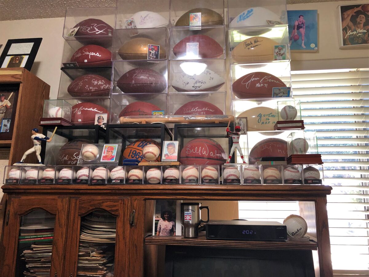 Rick Obrand has piles of sports documents stored on shelves below a display of autographed memorabilia at his home.