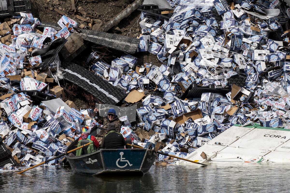 Fishermen in a boat claim a bottle of beer from a derailed railcar on the banks of a river.