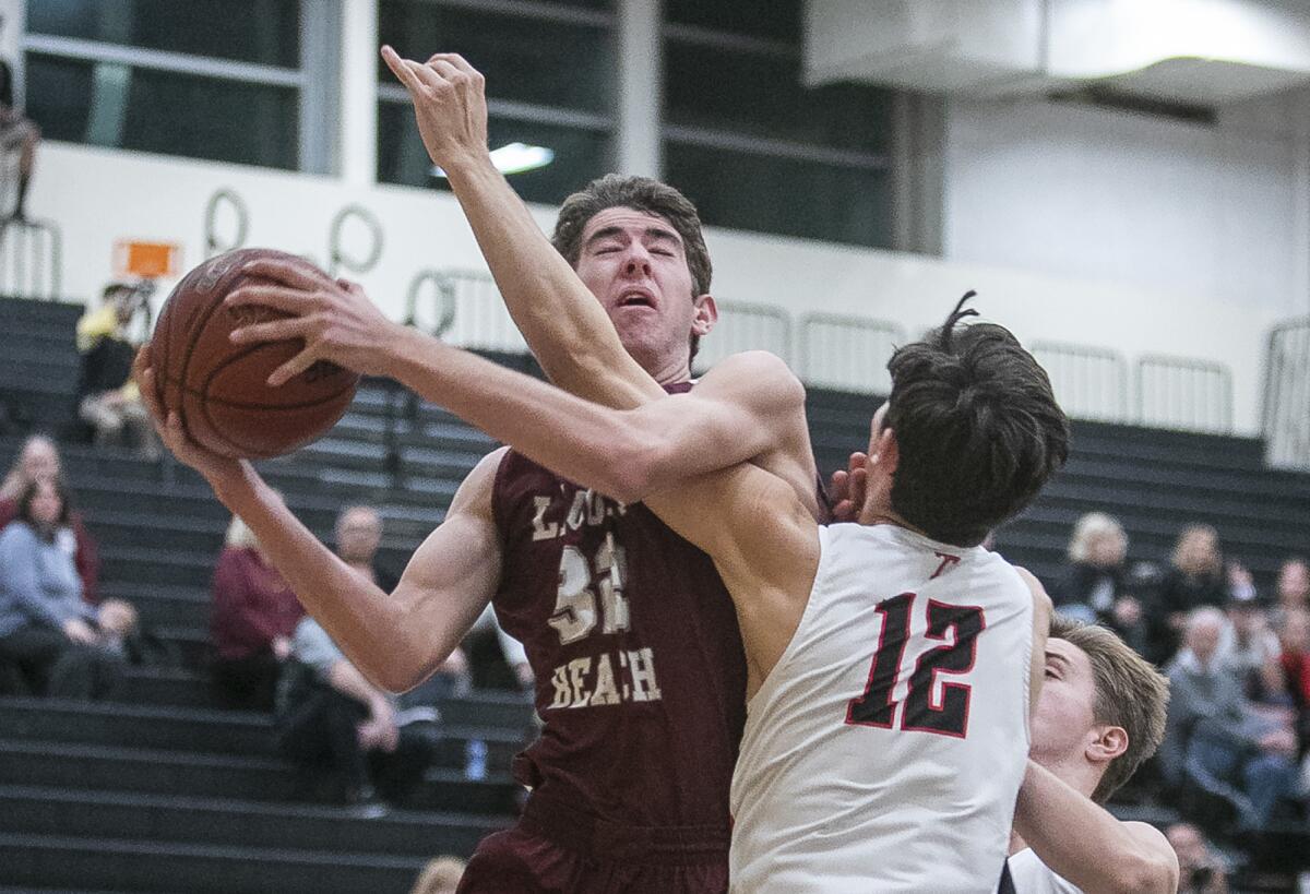 Laguna Beach's Nolan Naess, left, gets fouled by San Clemente's Micah Regalado while going up for a shot in the Grizzly Invitational Thursday at Godinez High.