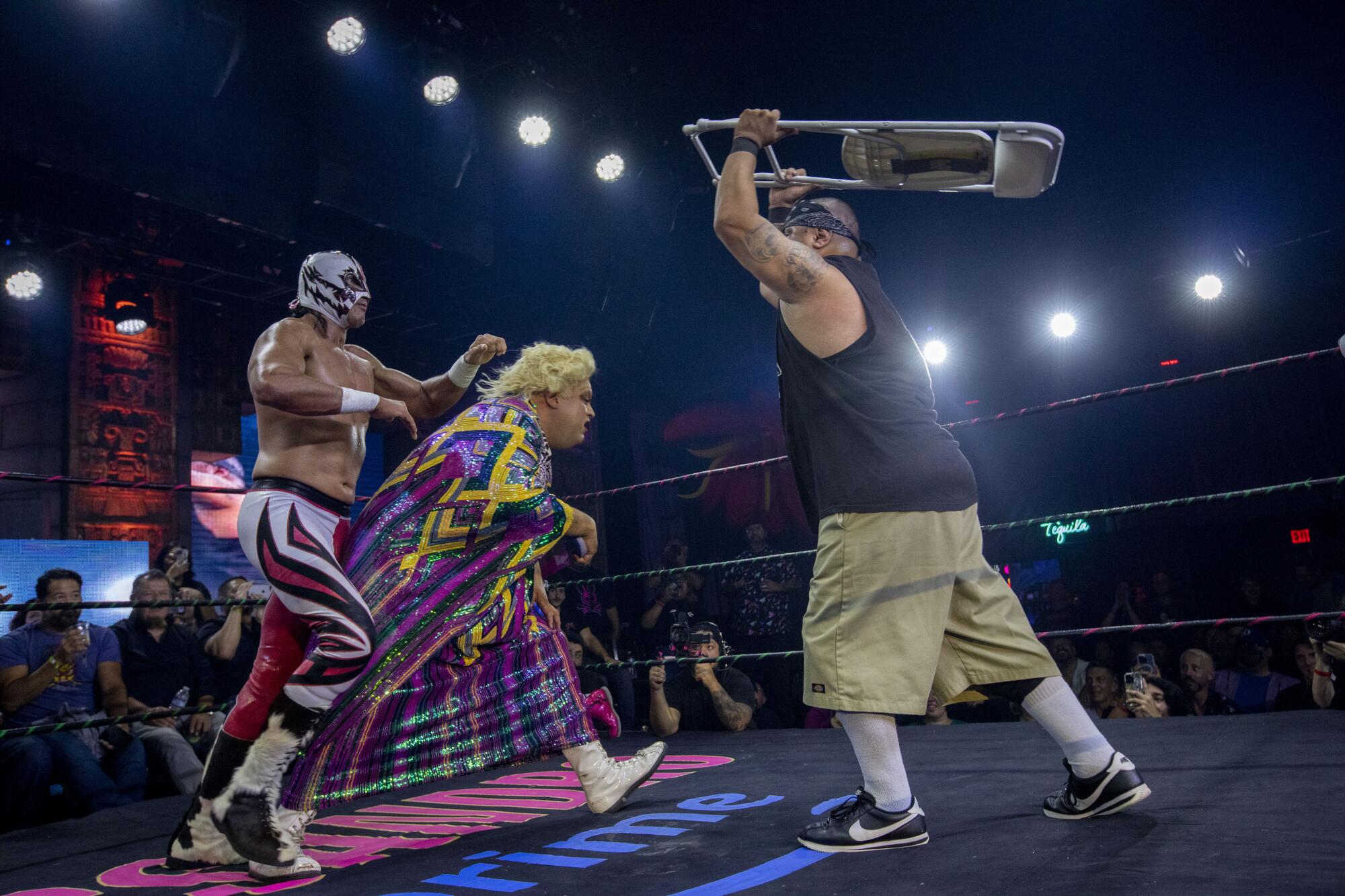 Li'l Cholo goes after Paquita with a chair 