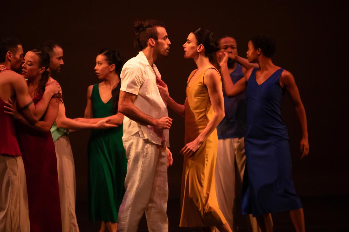 A group of dancers with a man and woman looking at each other in the center.