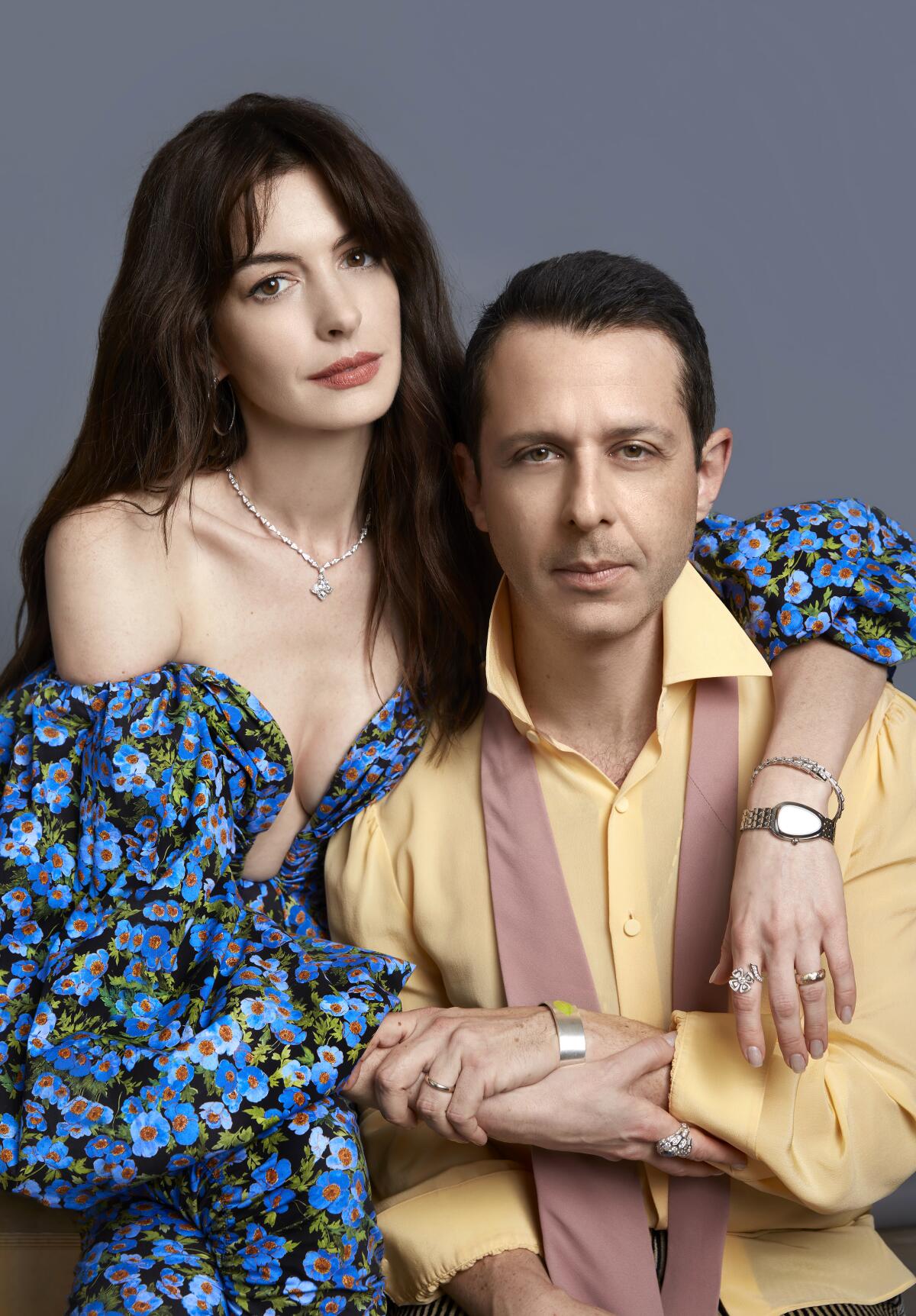 Anne Hathaway in a flowery dress poses for a portrait with her arms around Jeremy Strong.