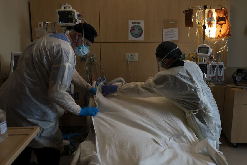 FILE - Respiratory therapist Frans Oudenaar, left, and registered nurse Bryan Hofilena cover a body of a COVID-19 patient with a sheet at Providence Holy Cross Medical Center in Los Angeles, Dec. 14, 2021. The fast-moving omicron variant may cause less severe disease on average, but COVID-19 deaths in the U.S. are climbing and modelers forecast 50,000 to 300,000 more Americans could die by the time the wave subsides in mid-March. (AP Photo/Jae C. Hong, File)