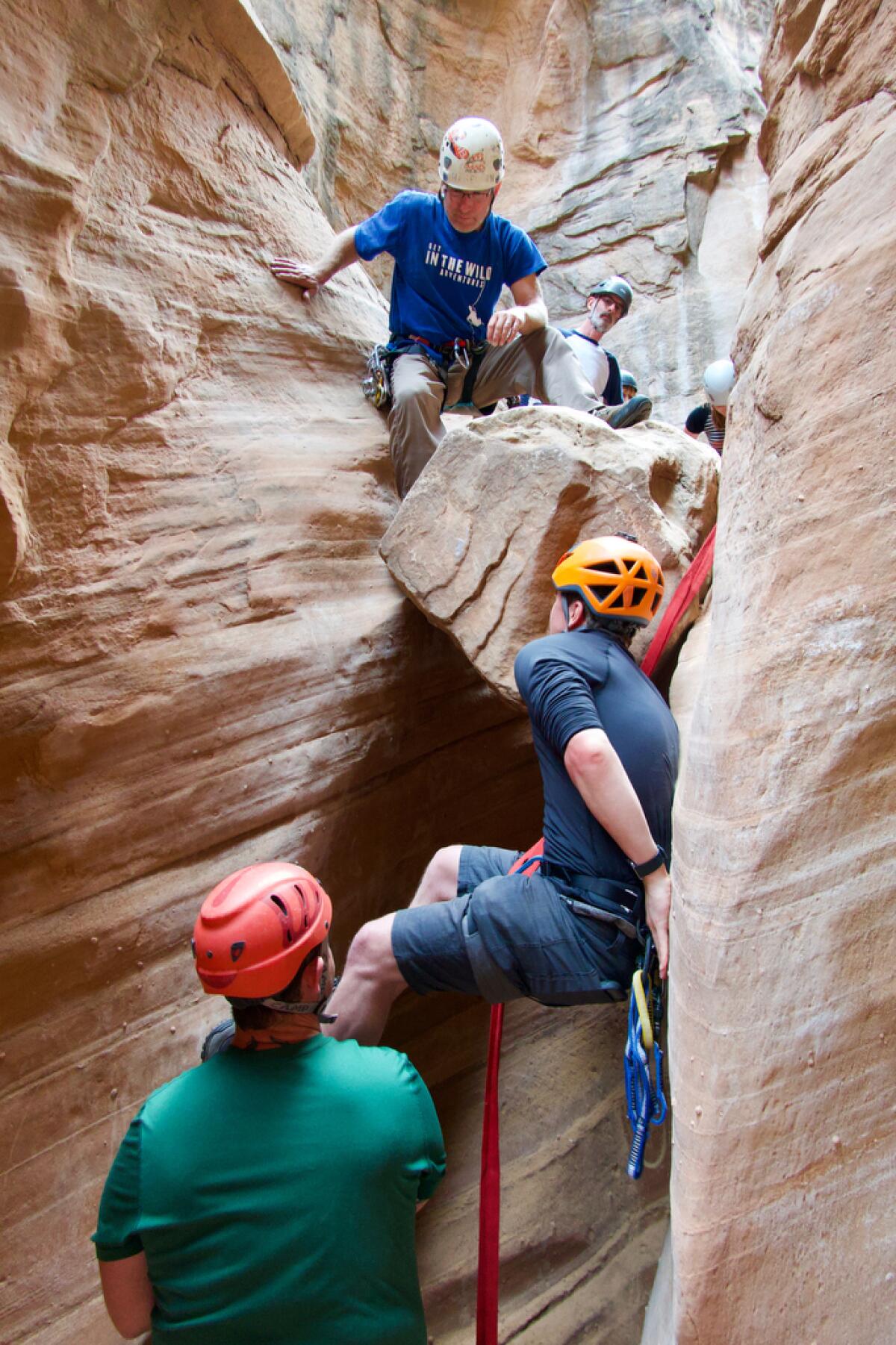 Students clamber up the steep sides of a slot canyon in Utah.