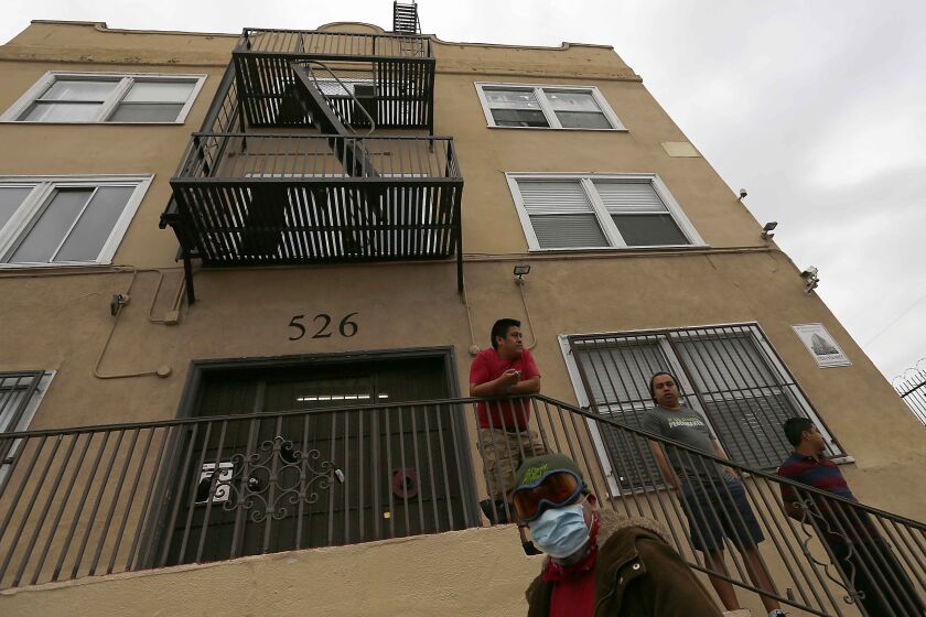 LOS ANGELES, CALIF. - APR. 18, 2020. Men stand outside an apartment building in the Westlake District of Los Angeles, which has the second highest population density in the city, with about 38,214 people per square mile. (Luis Sinco/Los Angeles Times)