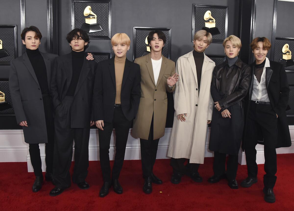 Seven fashionably dressed young men pose for a photo on a red carpet.