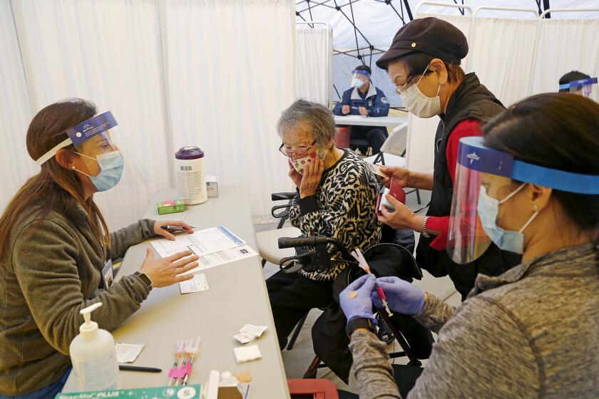 Huntington Beach Hospital registered nurse Nicole Lopez, left, goes over a few general health questions with Hideko Yamada, second from right, about her aunt Teruko Yamada, 101, center, as Garden Grove Hospital & Medical Center registered nurse Natalie Ambroff, far right, prepares to administer a COVID-19 vaccine at Huntington Beach Hospital mobile clinic on Friday morning.
