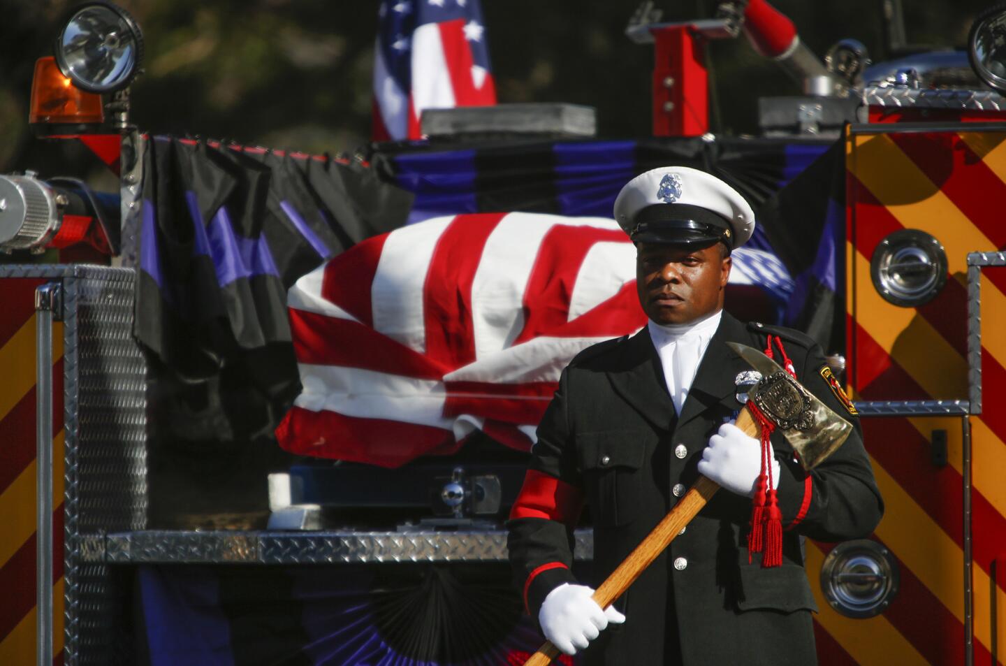 An honor guard stands at attention with an ax at the rear of the firetruck carrying the flag-draped coffin of fallen LAFD firefighter Kelly Wong at the Cathedral of Our Lady of the Angels.