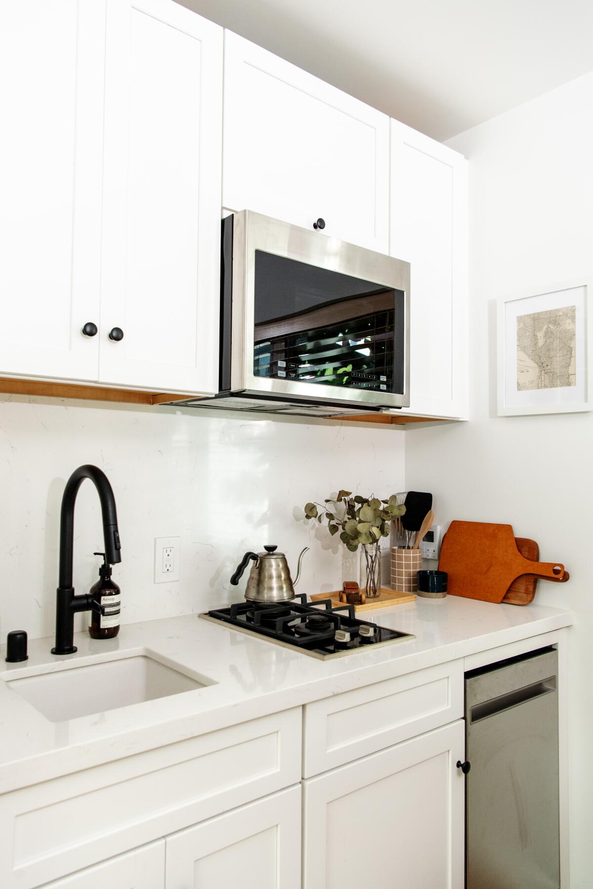 White cabinets fill this tiny kitchen with a silver microwave and dishwasher. 