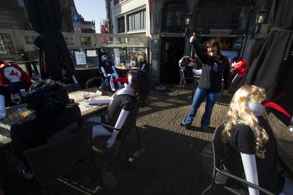 Cafe De Ooievaar owner Mary Schepers flashes a thumbs up to passing customers on her terrace filled with inflatable dolls in Delfshaven, Rotterdam, Netherlands, Tuesday, March 2, 2021. Stores in one village opened briefly, cafe owners across the Netherlands were putting tables and chairs on their outdoor terraces and sex workers were planning a demonstration outside parliament in protests against the government's tough coronavirus lockdown. (AP Photo/Peter Dejong)