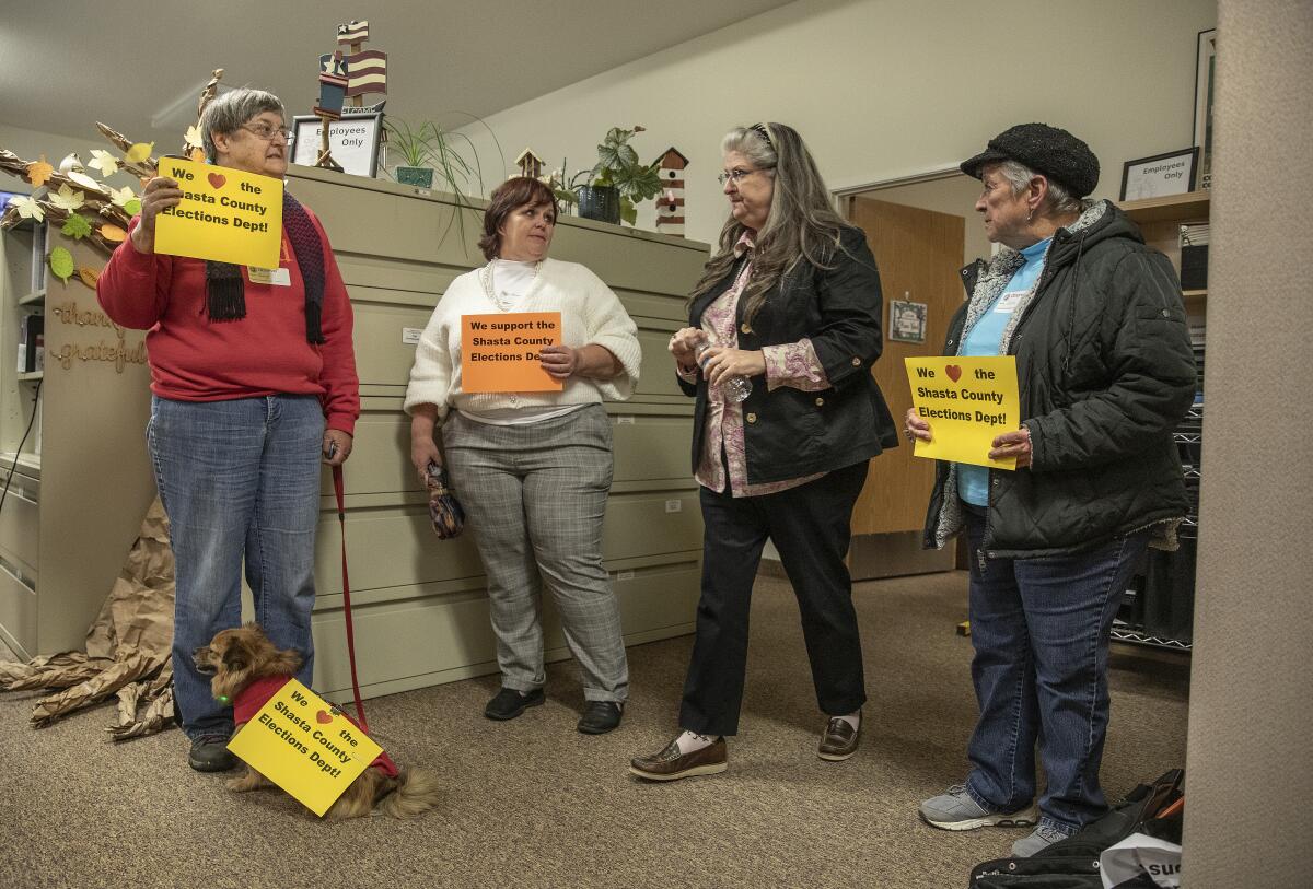 Four people hold signs in an office.