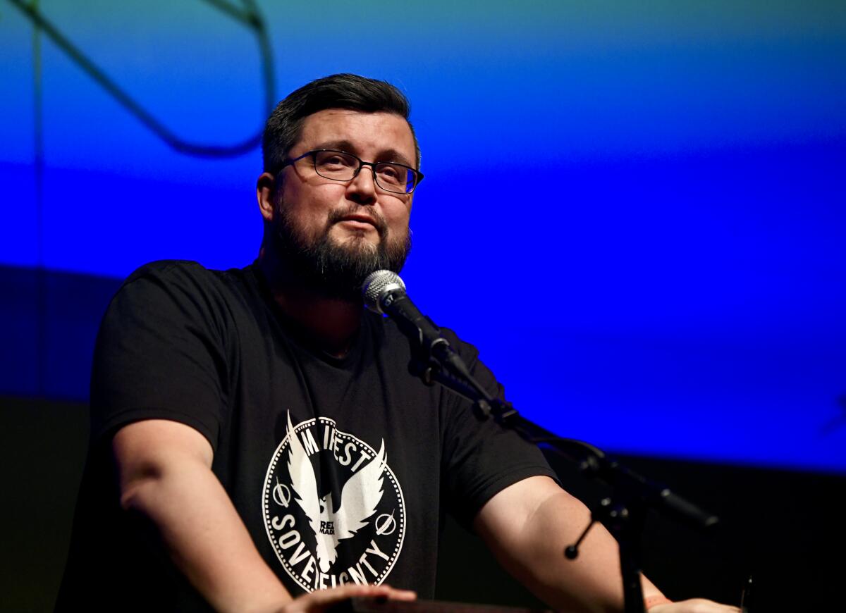 Sterling HolyWhiteMountain speaks at a lectern in front of a video screen