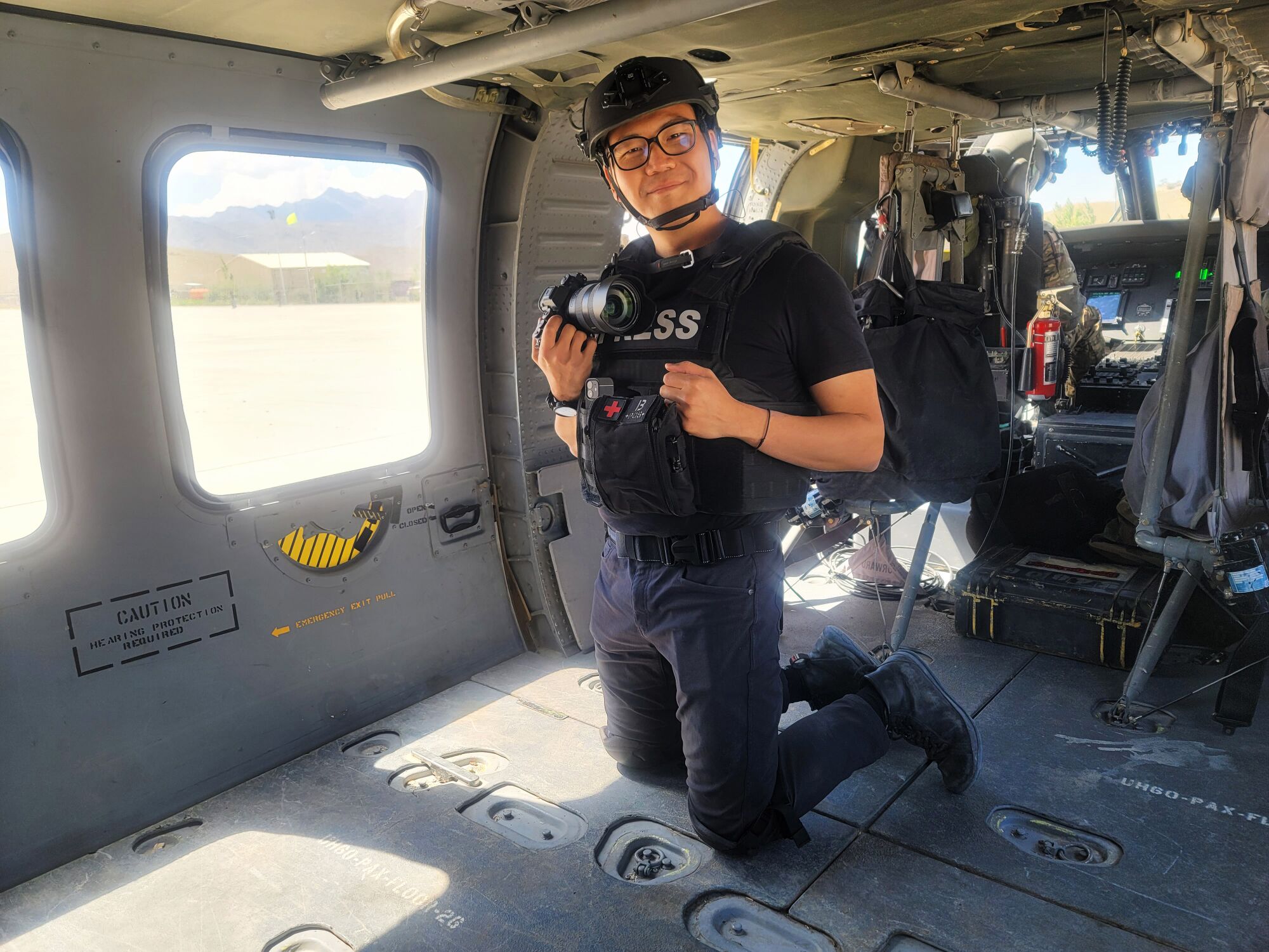 A man kneeling and smiling while holding a camera in a helicopter.