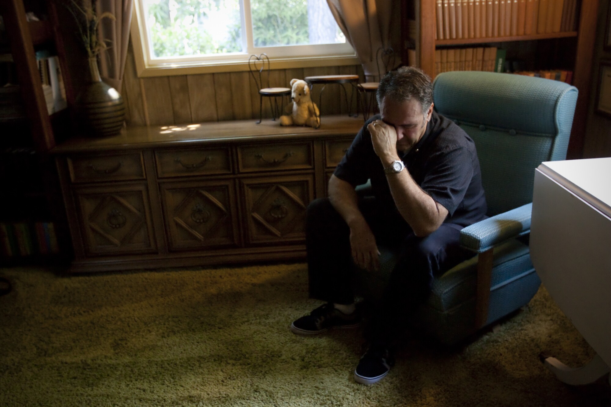 A man sits in a dark room, wiping his eyes