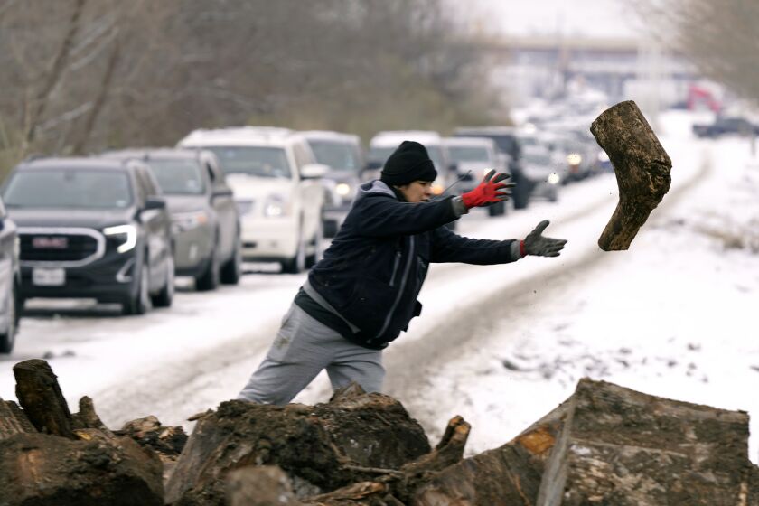 Michelle Terrazas tosses a log of firewood as as people line up to load up Wednesday, Feb. 17, 2021, in Dallas. (AP Photo/LM Otero)