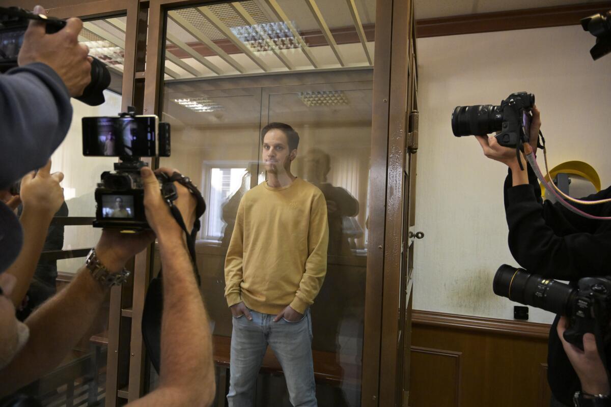 Wall Street Journal reporter Evan Gershkovich stands in a glass cage in a courtroom in Moscow.