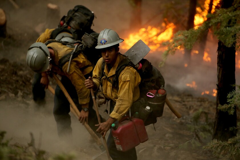 A team of firefighters at work with flames in the close background.