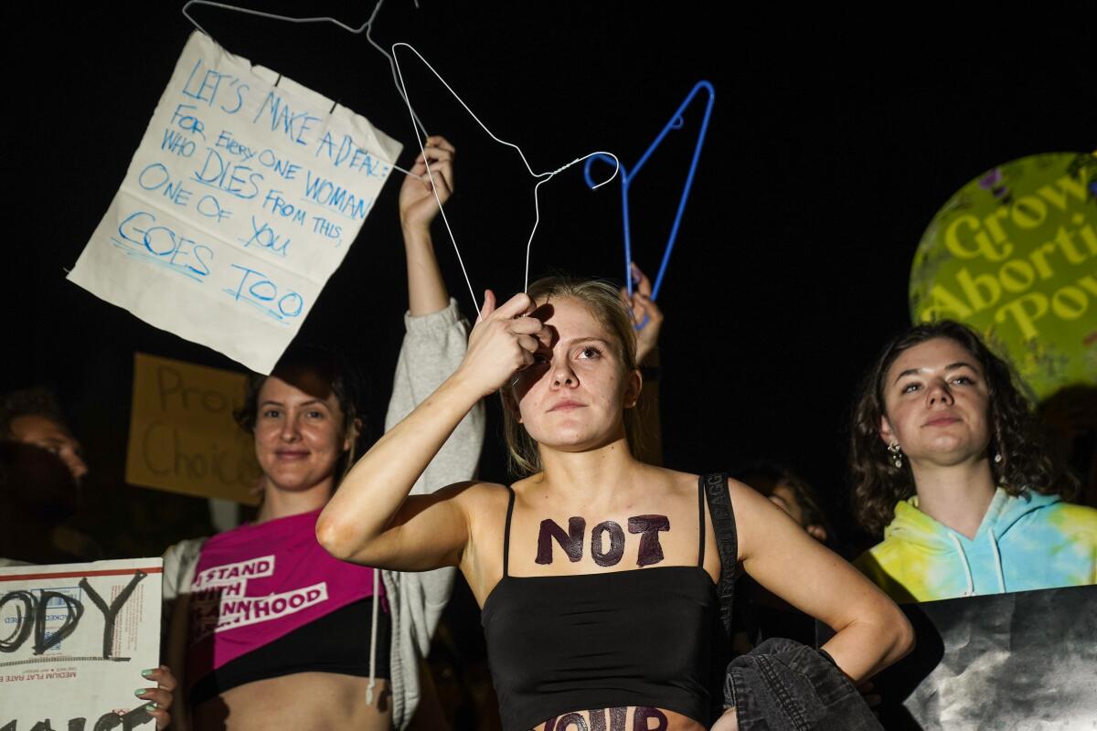 From left: a woman holds a sign; a woman with the word "not" on her chest scratches her forehead; and a woman stands 