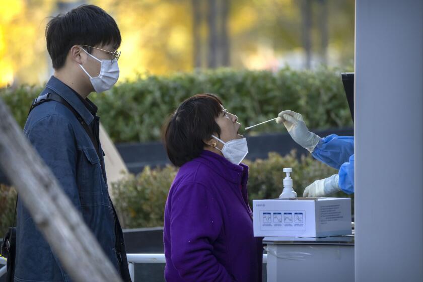 A woman has her throat swabbed for a COVID-19 test at a coronavirus testing site in Beijing, Friday, Nov. 4, 2022. Chinese stocks in Hong Kong gained Friday after the health ministry said the mainland's severe anti-virus controls should be less costly and disruptive and a city said it would ease restrictions after access to an area around the world's biggest iPhone factory was suspended. (AP Photo/Mark Schiefelbein)