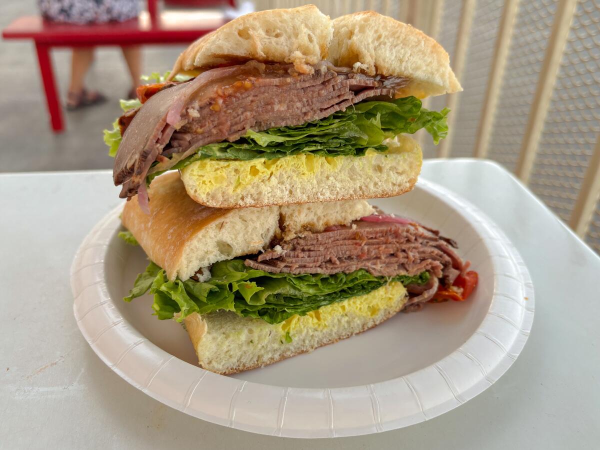 A roast beef sandwich on a paper plate, its halves stacked