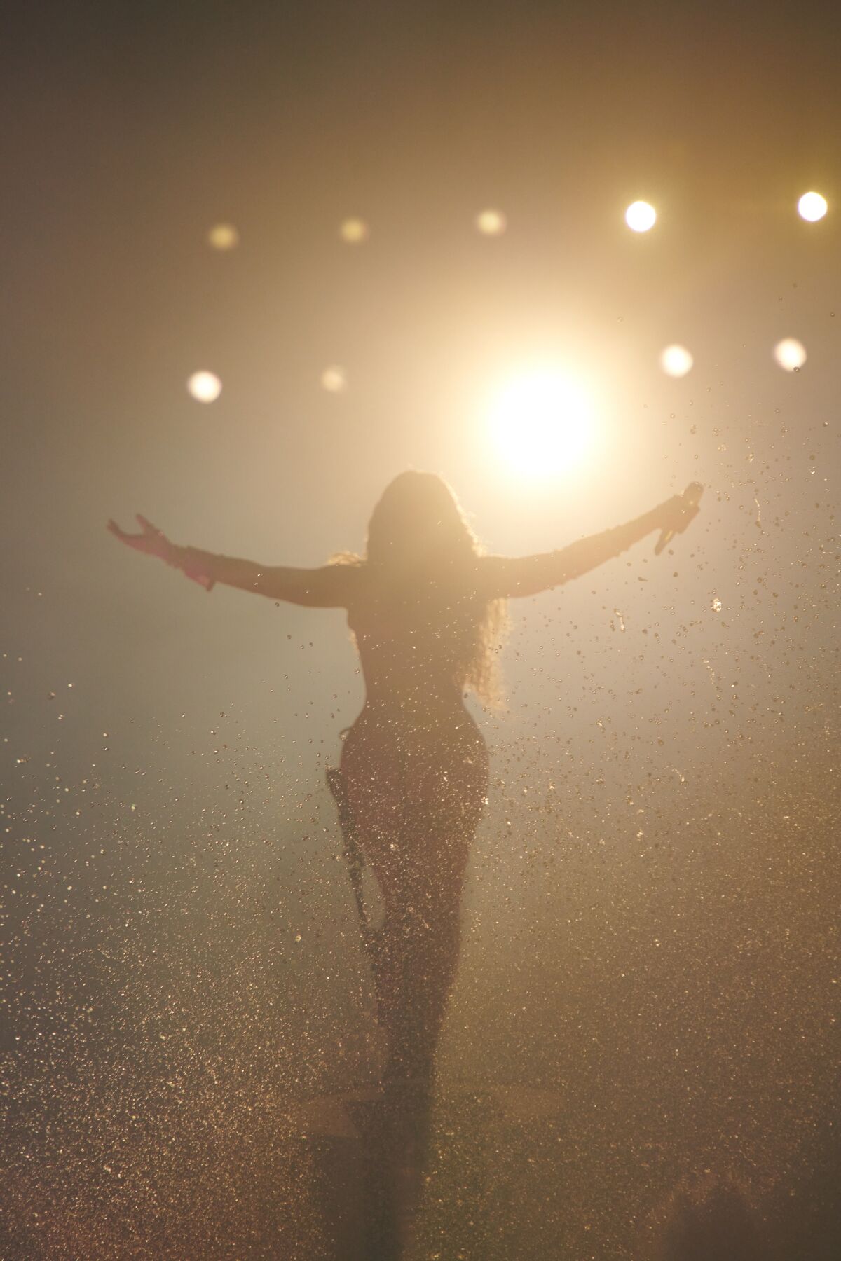 Silhouette of a woman with arms open in front of stage lights