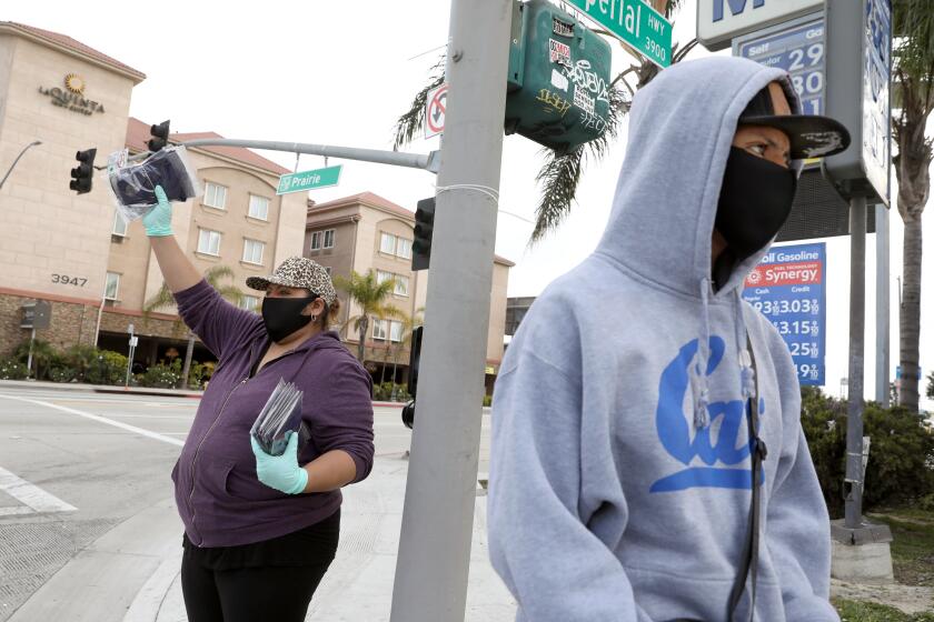 HAWTHORNE, CA -- APRIL 04: Brenda Mendez, left, with son David Mendez, 16, of Redondo Beach, sell mask along Prairie Ave. on Saturday, April 4, 2020, in Hawthorne, CA. Brenda Mendez was laid off from work and has resorted to selling face masks with her son David for $5 a piece to try and make an income due to coronavirus. (Gary Coronado / Los Angeles Times)