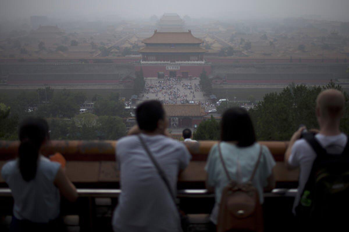 Tourists look at the Forbidden City from the top of Jinshan Hill on a hazy day in Beijing