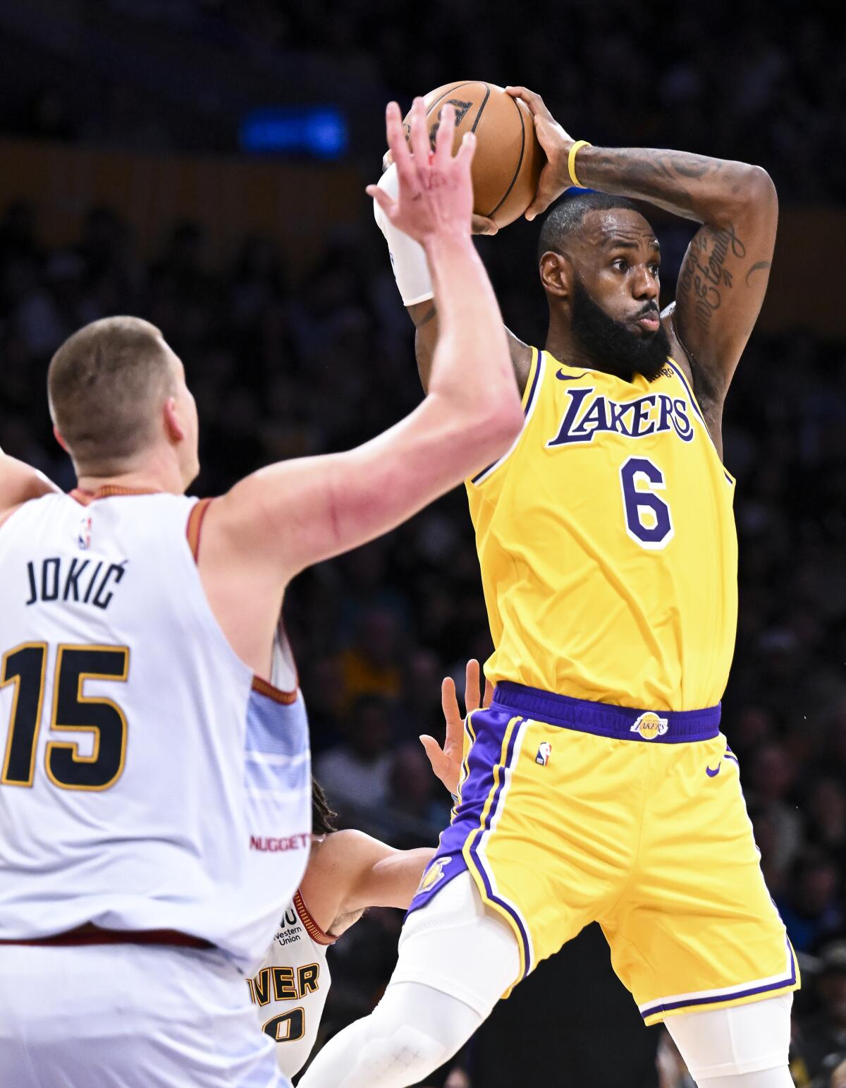 Lakers forward LeBron James, right, leaps to make a pass while defended by Nuggets center Nikola Jokic.
