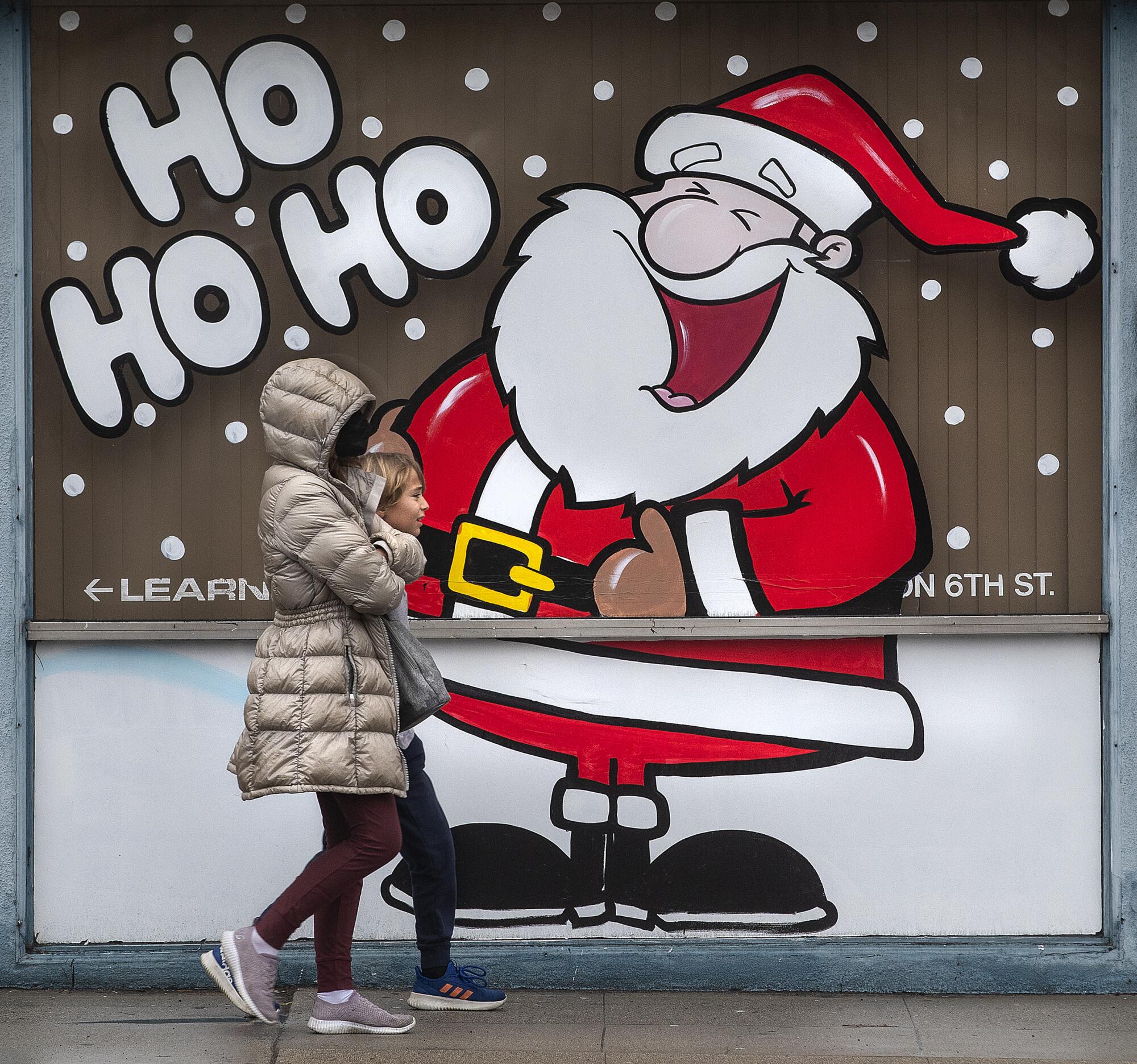 Pedestrians walk past a storefront with a cartoon of Santa Claus and the words "Ho ho ho"