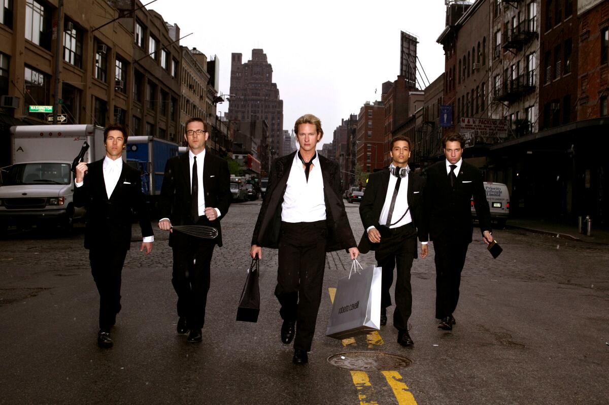 Five men in black suits and white shirts walk down the middle of a New York City street.