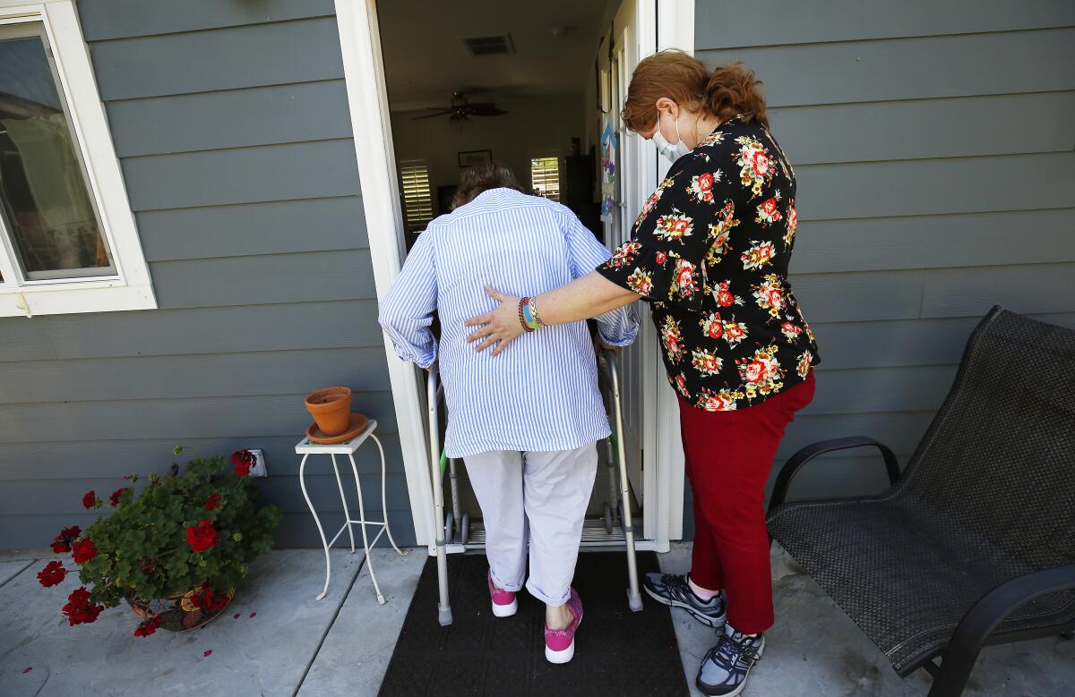 A care provider helps a client walk into a home.