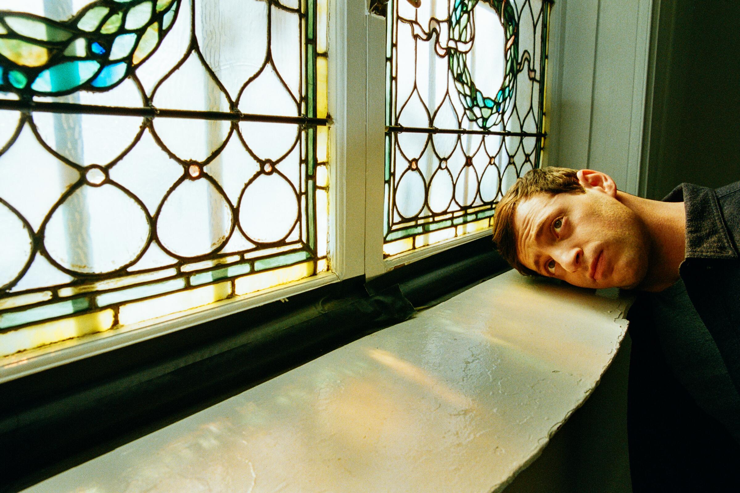 A man places his head on a windowsill.