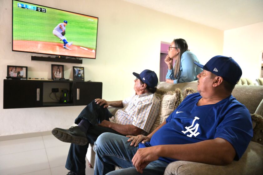 Culiacan, Mexico August 28, 2022-Carlos Urias, right, with grandfather Julian and mother Juana Isabel Acosta watch as Dodgers pitcher Julio pitches on the television during a recent game against the Marlins. (Wally Skalij/Los Angeles Times)
