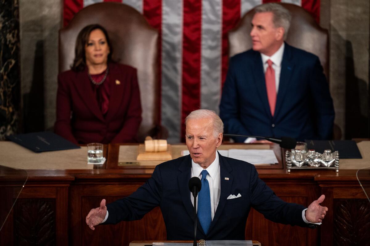 President Biden speaking at the Capitol, arms outstretched, as Kamala Harris and Kevin McCarthy sit on the dais behind him