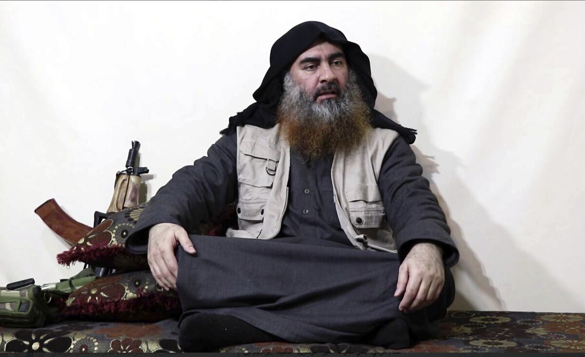 A man sits cross-legged with a weapon next to him.
