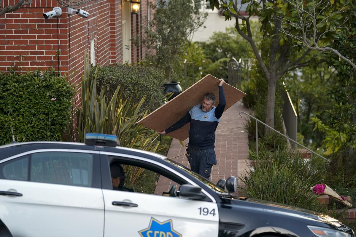 A worker carries a sheet of plywood from the home of Paul Pelosi