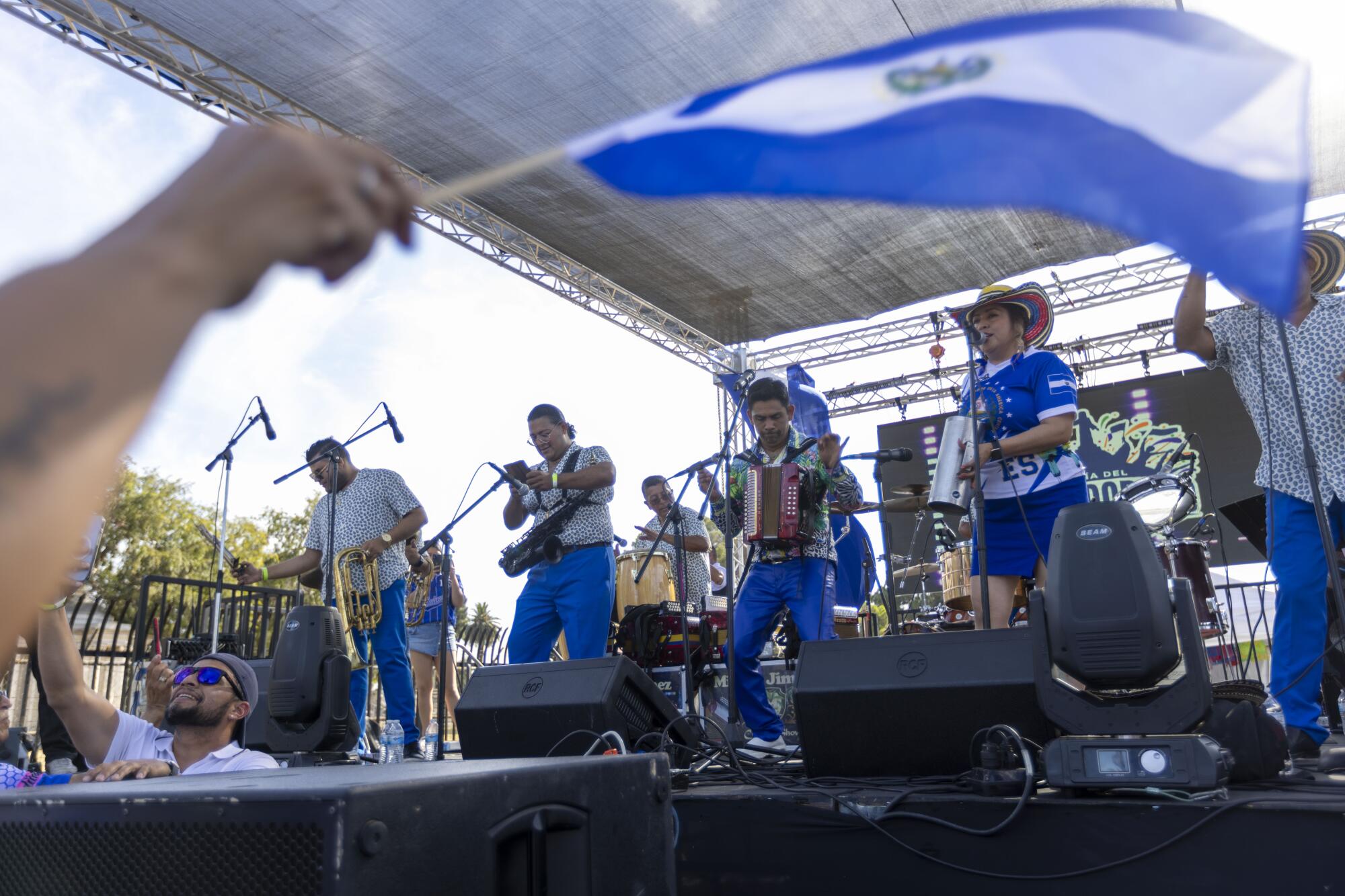 Una persona de la multitud ondea una bandera salvadoreña mientras Miguel Jiménez y su Cumbia Show ac