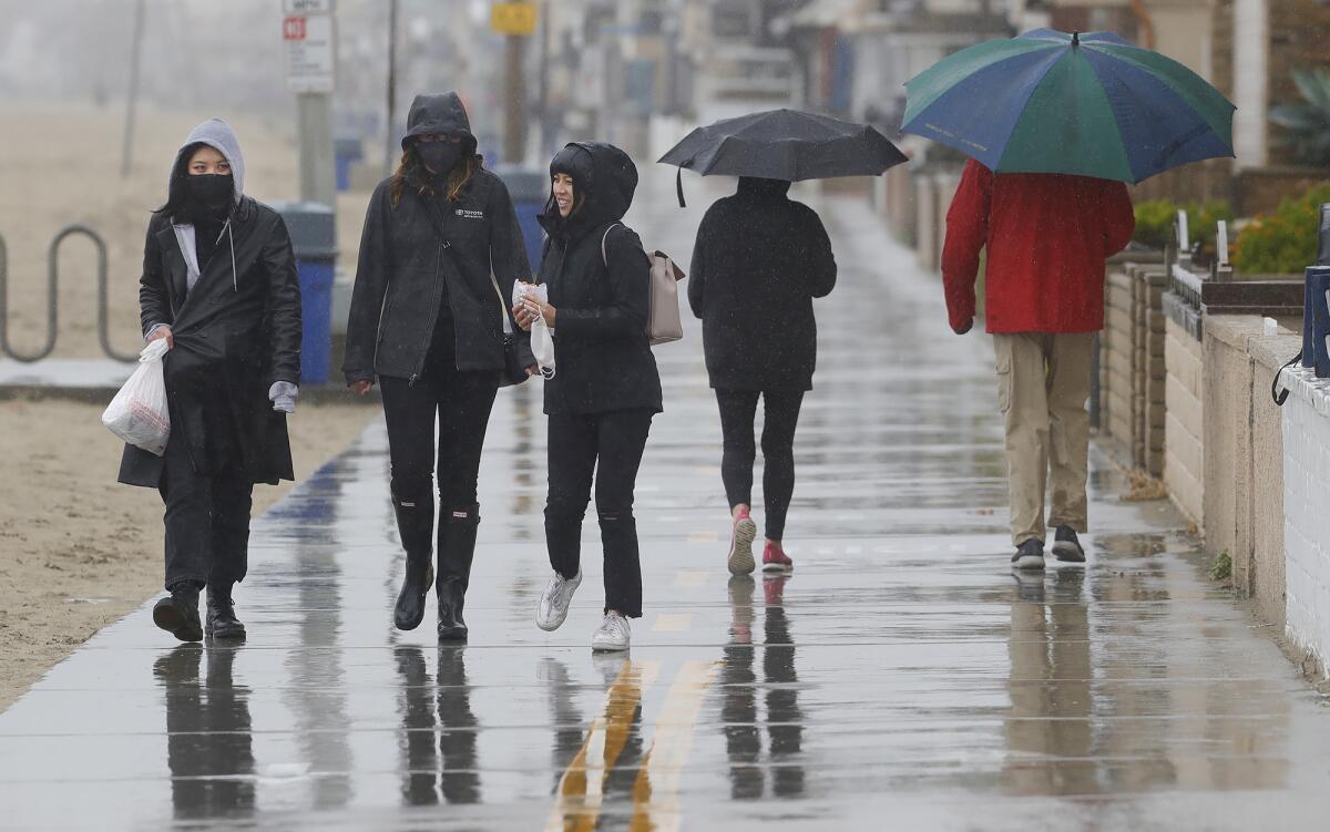 Three college friends from Colorado brave the rain Thursday as they walk along the boardwalk in Newport Beach.
