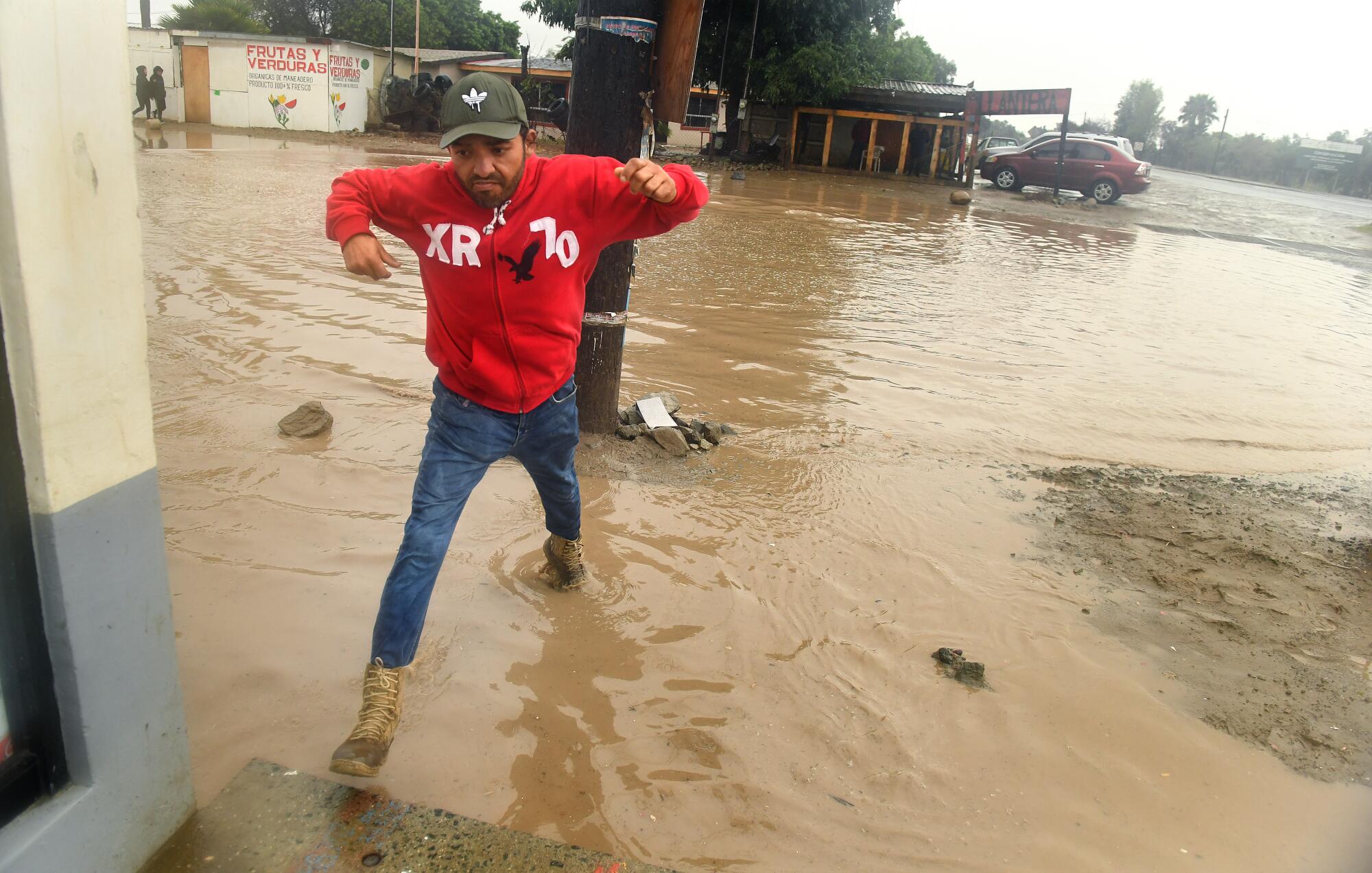 A man takes large steps to avoid getting wet in a giant puddle of muddy water.