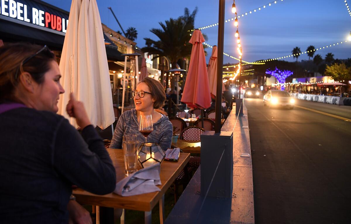 Outside a restaurant, a masked hostess takes a customer's temperature using a forehead thermometer.