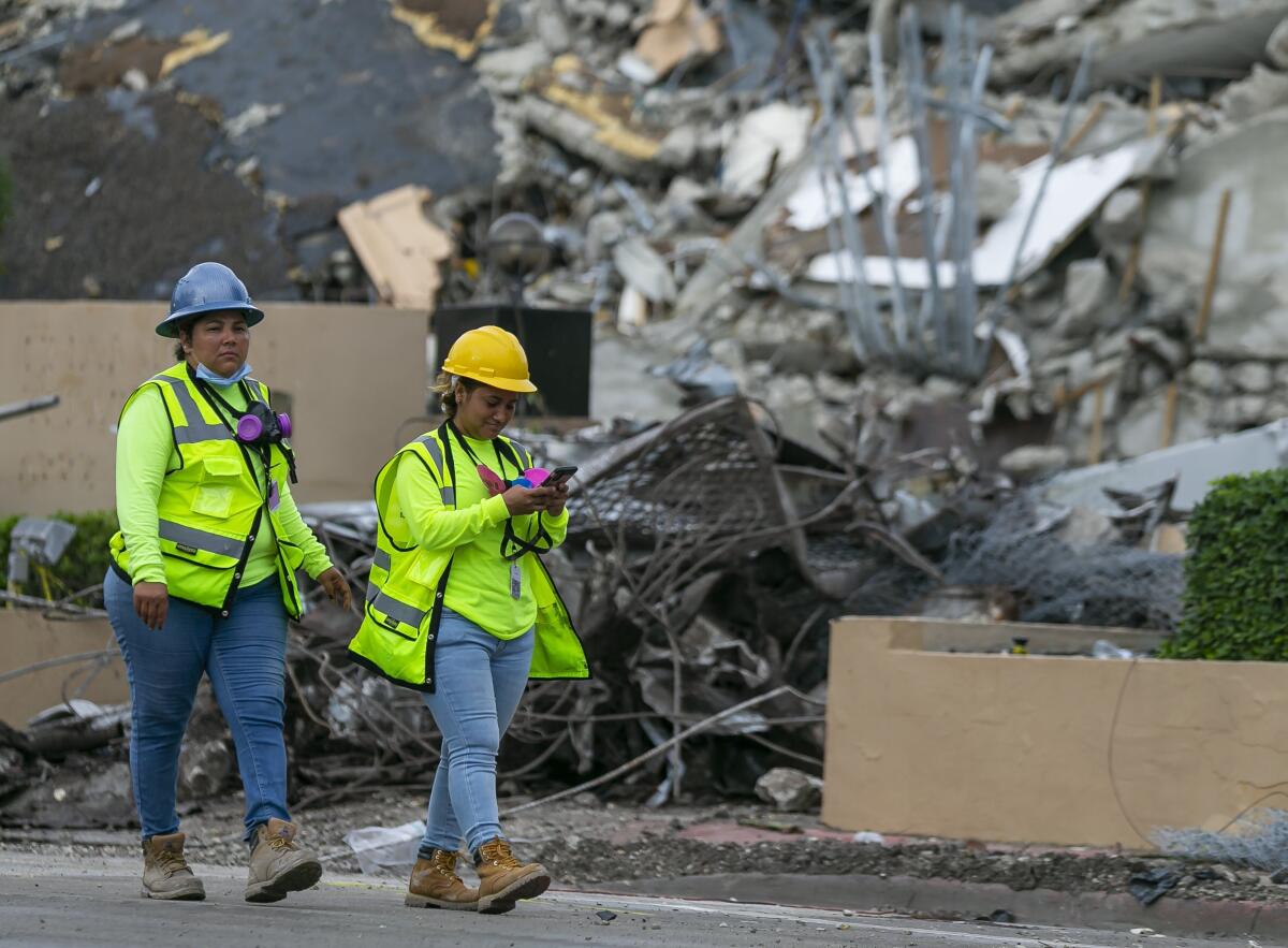 Workers in hard hats walk past a mountain of rubble.