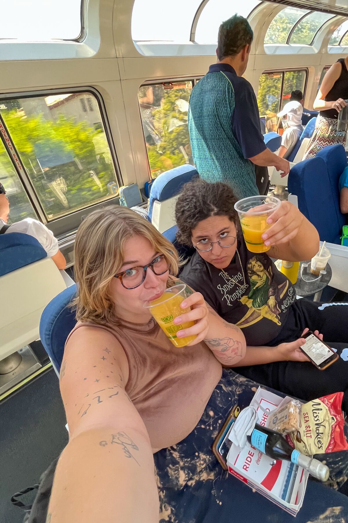 two women take a selfie holding drinks in a train