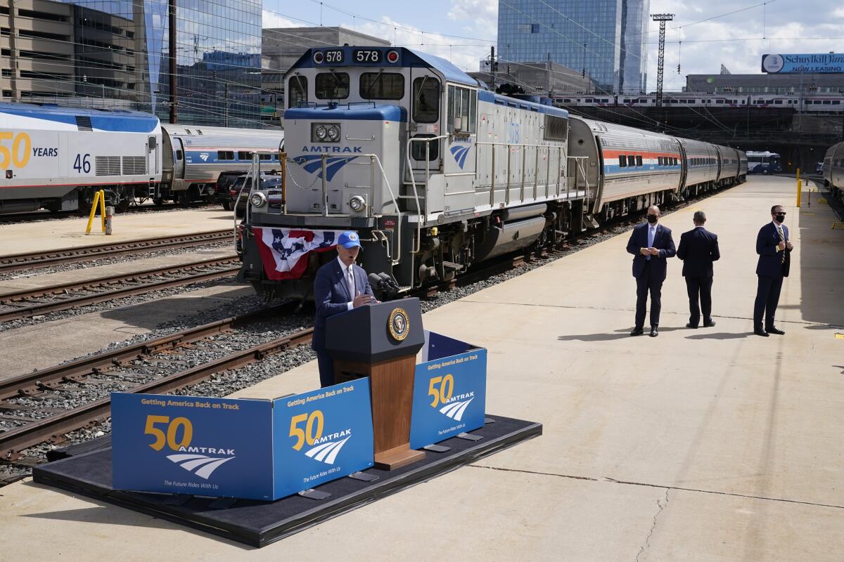 President Biden stands at a small podium set up trackside in front of locomotive and train