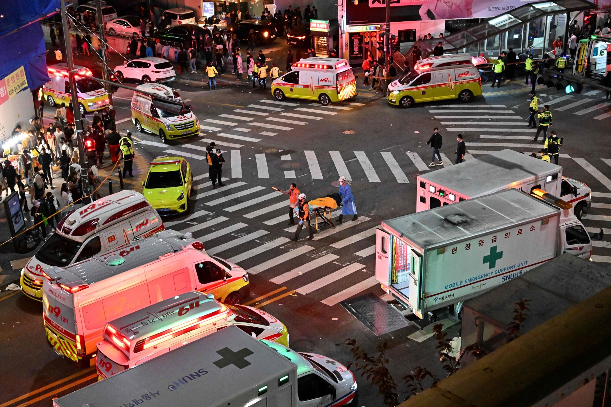 Emergency vehicles are parked around an intersection in which a person is transported on a gurney. 