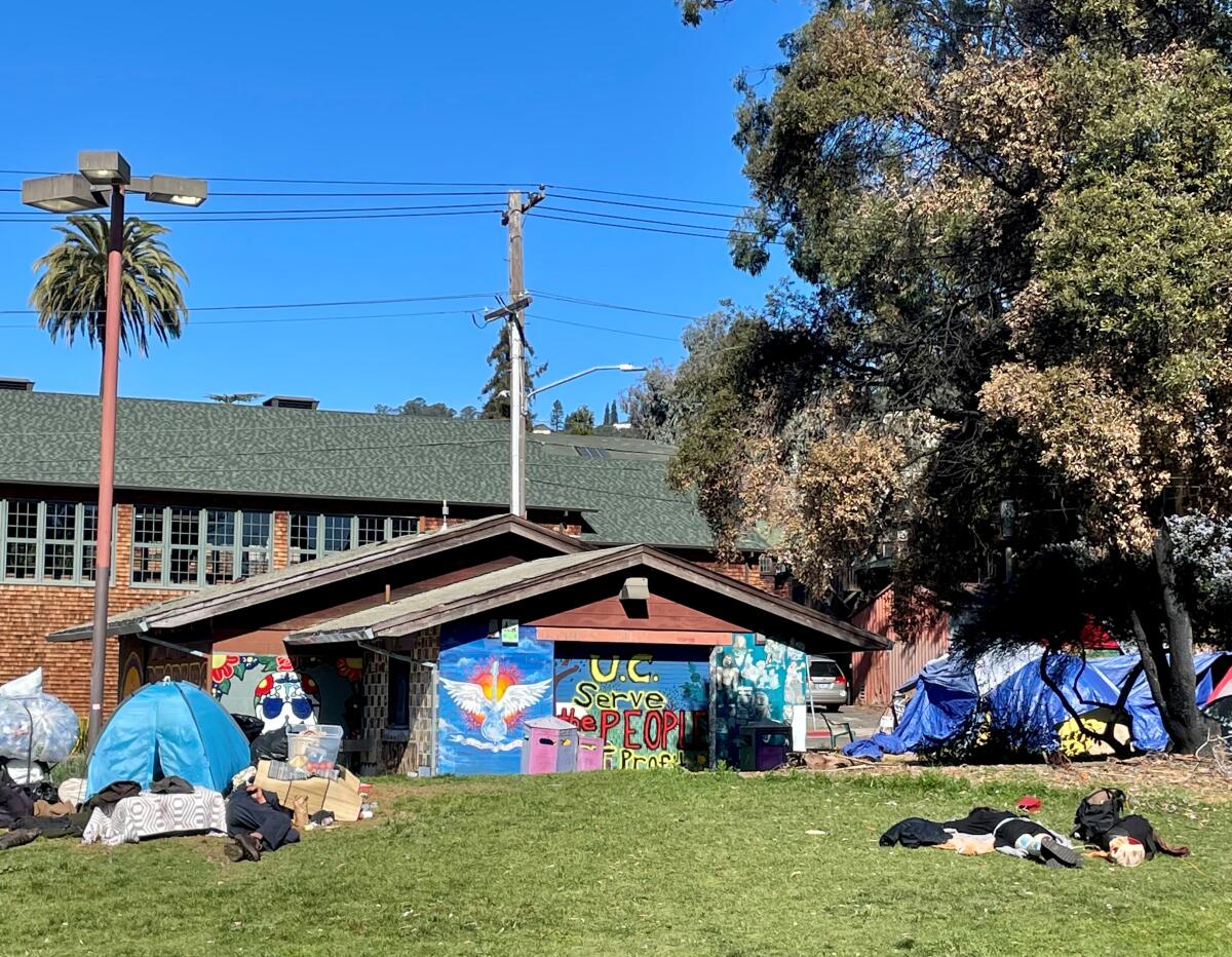 Unhoused people sleep in People's Park near tents and buildings.