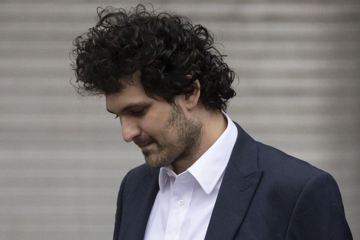 A curly-haired man in a suit jacket and a white shirt looks down.