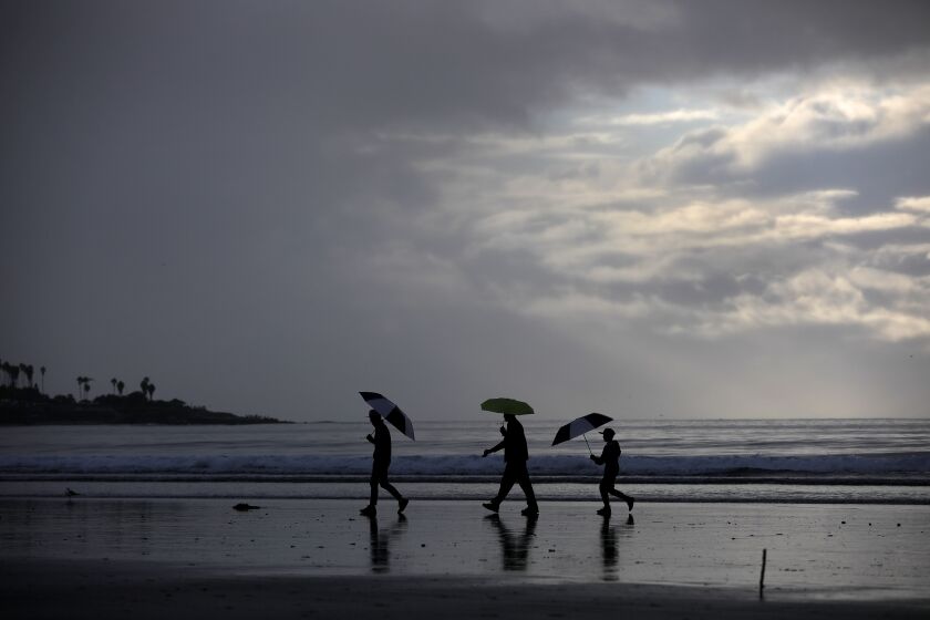 People walk on the sand as it rains at La Jolla Shores on Dec. 23, 2019.